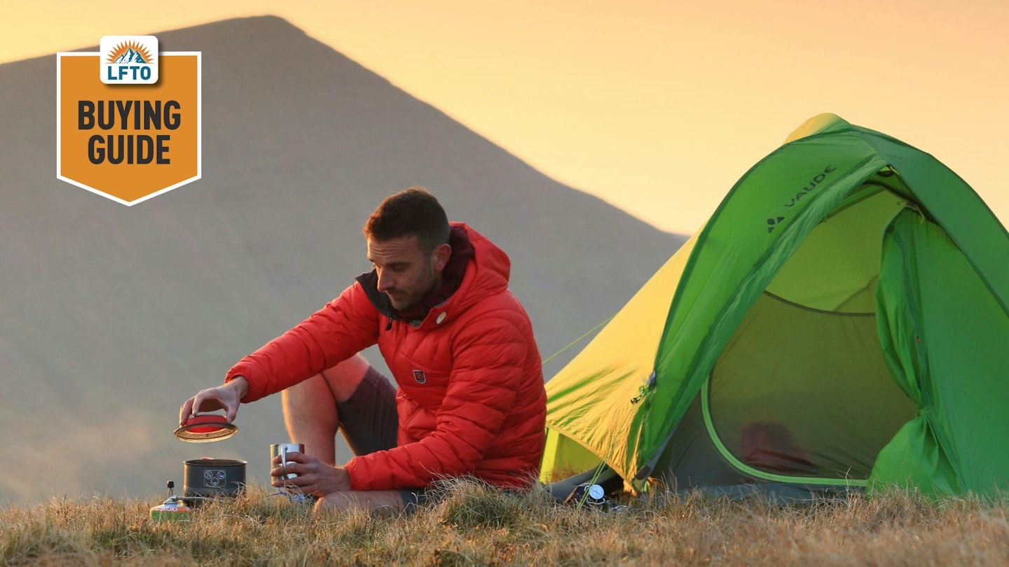 backpacking stove buying guide main image, showing a man cooking next to a tent